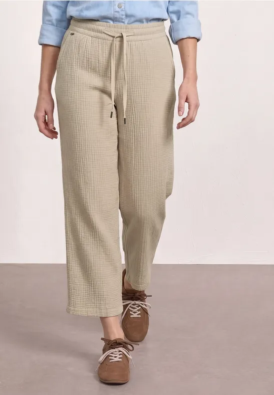 Benedenlichaam in beige, wijde enkelhoge linnenbroek met koordsluiting en bruine sneakers