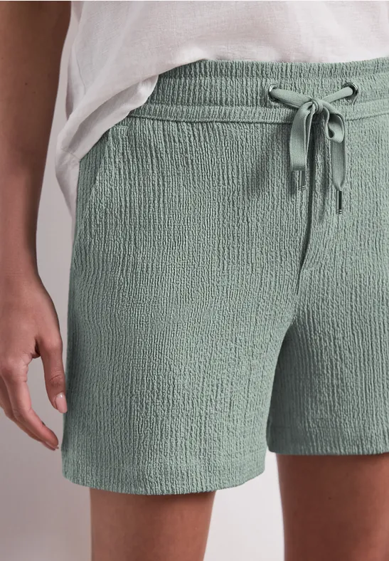 Vue rapprochée d'une personne portant un short vert pâle texturé avec cordon et un haut blanc.