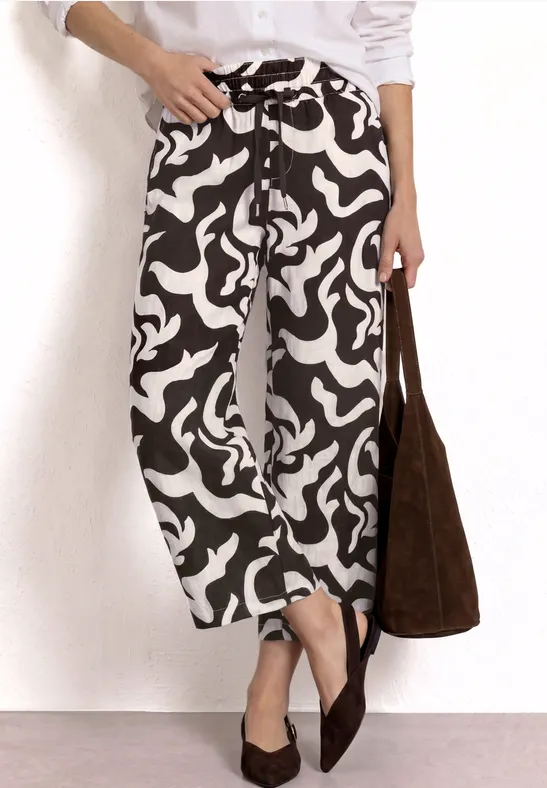 Witte top, zwarte-wit patroon broek, bruine tas, puntige platte schoenen.