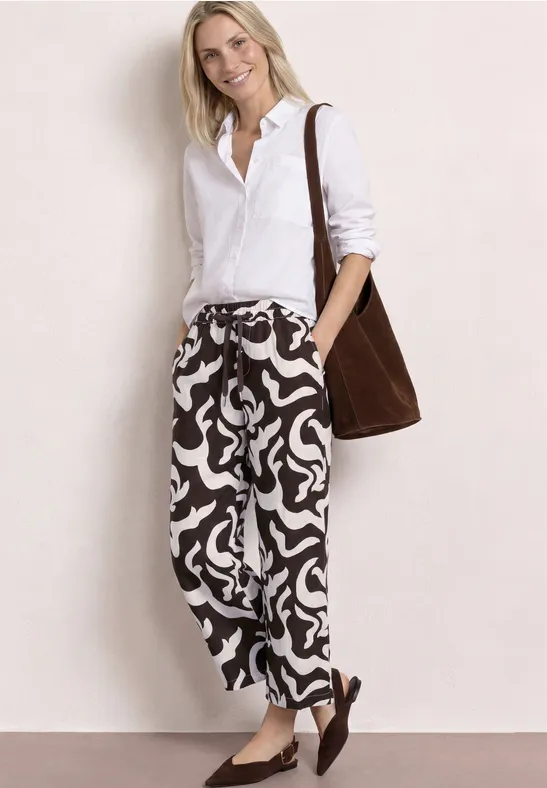 Vrouw met wit overhemd, abstracte gemêleerde broek, bruine schoudertas en loafers