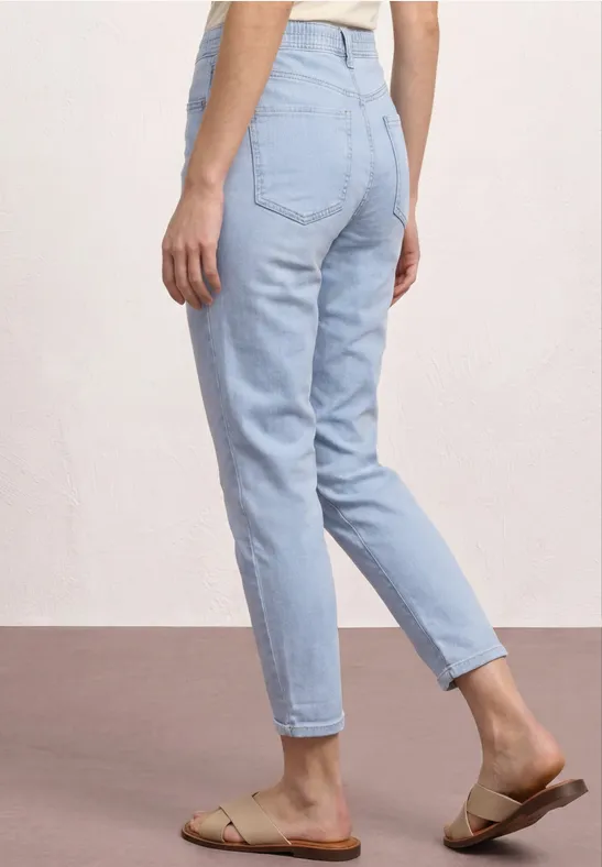 Frau von hinten in hellblauen Jeans und sandfarbenen Sandalen.