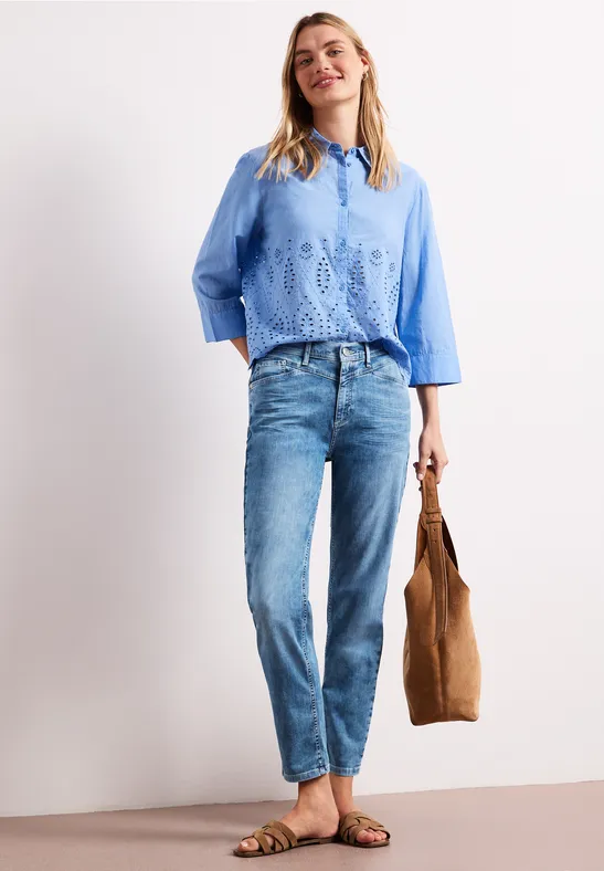 Vrouw in blauw gehaakt shirt, jeans en sandalen, met een bruine tas.