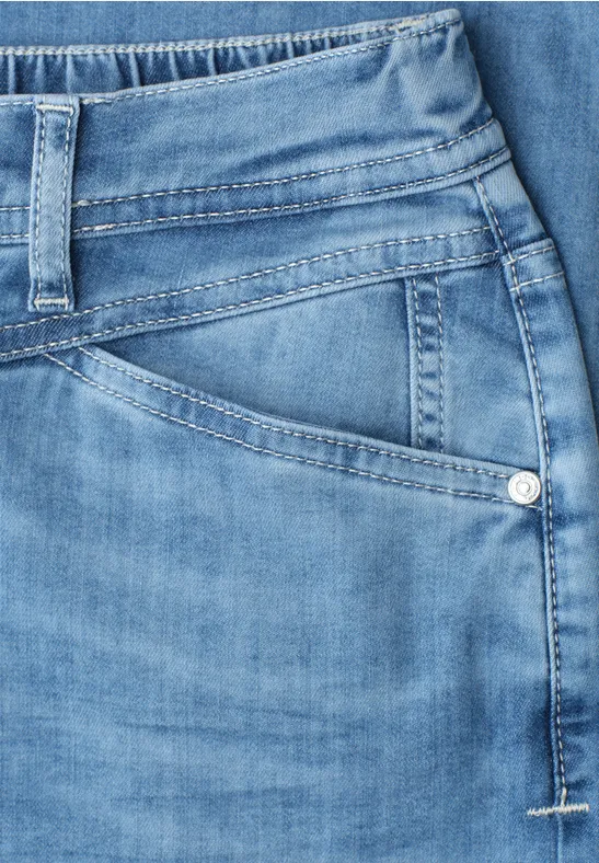 Close-up van een lichtblauwe spijkerbroekzak en tailleband met zichtbare stiksels en riemlussen.