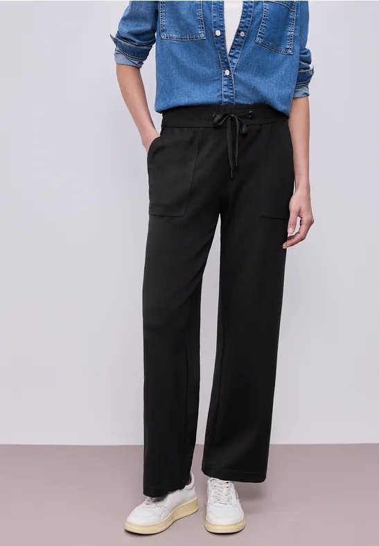 Modische schwarze, weit geschnittene Hose mit Tunnelzug, kombiniert mit Jeanshemd und weißen Sneakern.