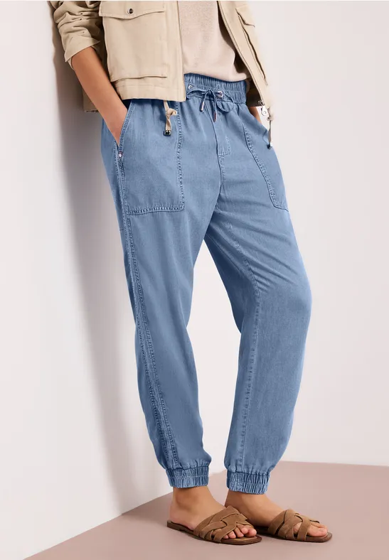 Losse lichtblauwe jogger met trekkoord, zijzakken en elastische boorden, gecombineerd met platte sandalen.