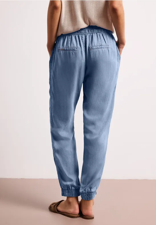 Rugaanzicht van een persoon in lichtblauwe joggingsbroek met elastische taille en sandalen.