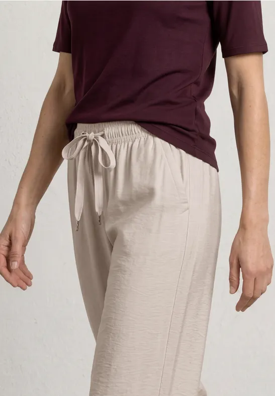 Persoon draagt licht linnen broek met trekkoord en bordeaux t-shirt op een effen lichte achtergrond.