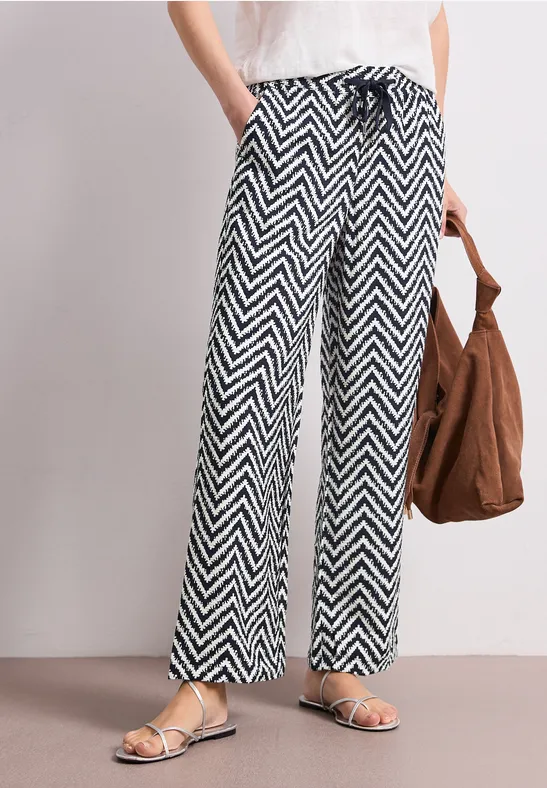 Vrouw draagt zwarte-witte zigzag wijd broek met trekkoord, sandalen en bruine tas