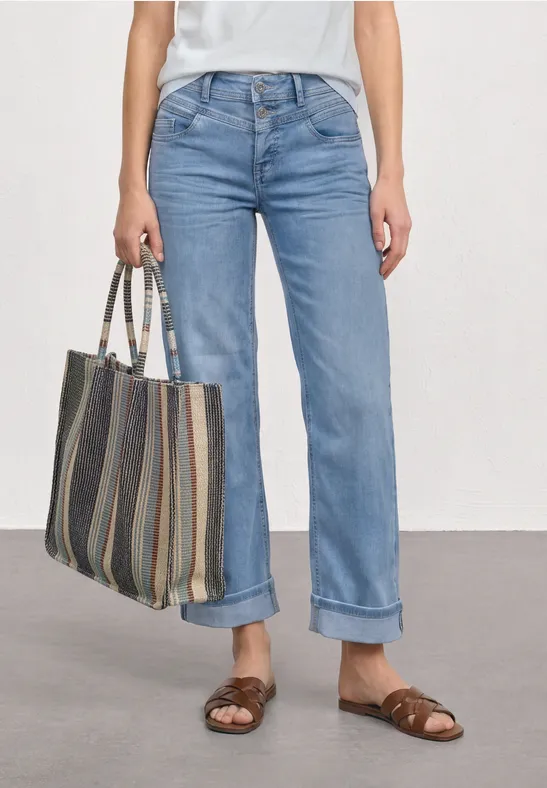 Vrouw met omgeslagen blauwe jeans, bruine sandalen en een gestreepte shopper.
