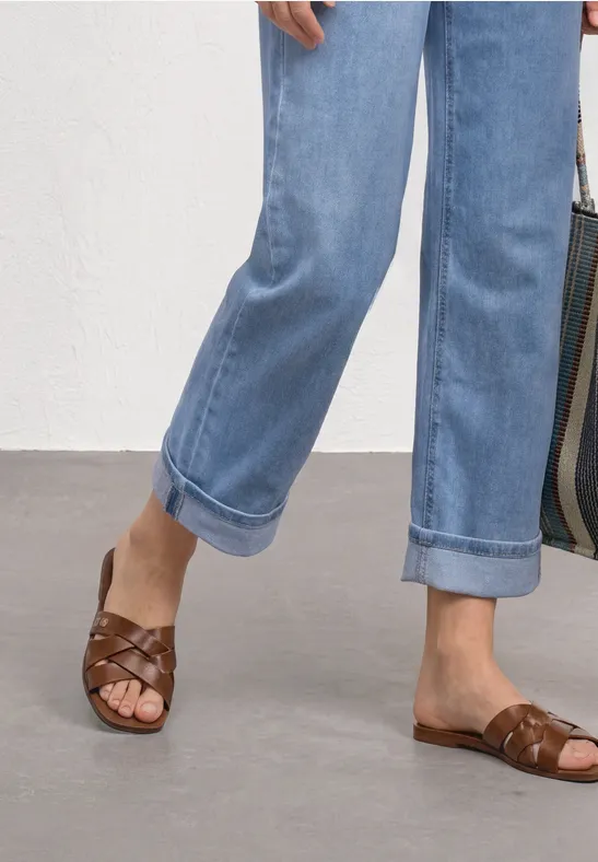 Voeten in gevlochten bruine leren sandalen en omgeslagen lichtblauwe jeans.