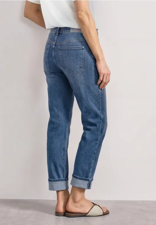 Rugaanzicht van iemand in blauw, recht gesneden jeans met omslag, witte sandaal en wit shirt.