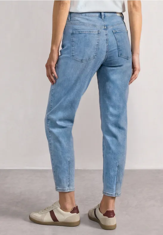 Vue arrière d'une personne portant un jean taille haute bleu clair et des baskets beiges à détails marron.