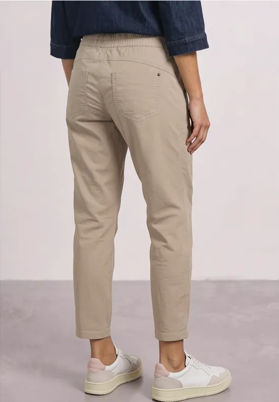 Persoon van achteren in beige chino's en witte sneakers voor een neutrale achtergrond.