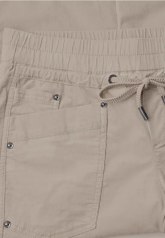 Beige broek met elastische taille, aantrekkoord en zak met metalen klinknagels.