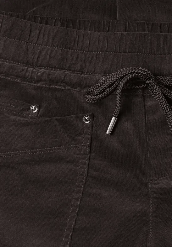 Zwarte fluwelen broek met elastische taille, trekkoord, zijzakken en metalen oogjes als subtiel detail.