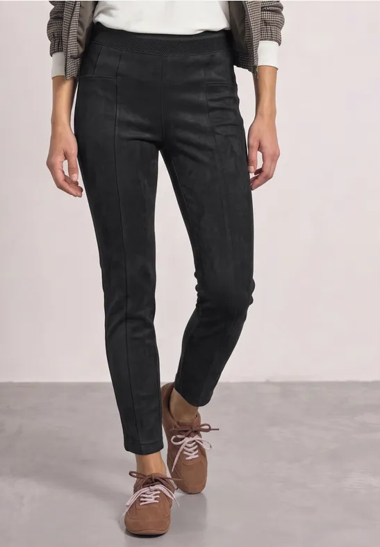 Person trägt schwarze, eng anliegende Hose und braune Schnürschuhe, steht auf grauem Boden.