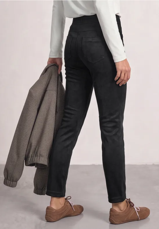 Person von hinten, trägt schwarze Hose, braune Schuhe und hält graue Jacke in der Hand.