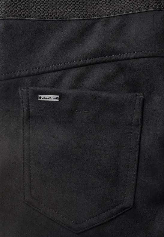 Nahaufnahme einer schwarzen Tasche mit sichtbaren Nähten und kleinem Metalllogo auf einem Kleidungsstück.
