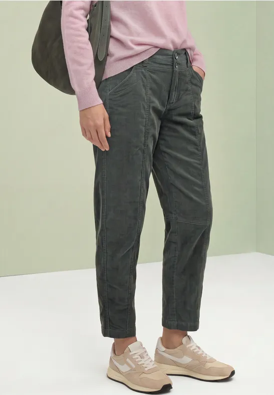 Personne porte un pull rose, un pantalon velours côtelé gris foncé, des baskets beiges et un sac bandoulière gris.