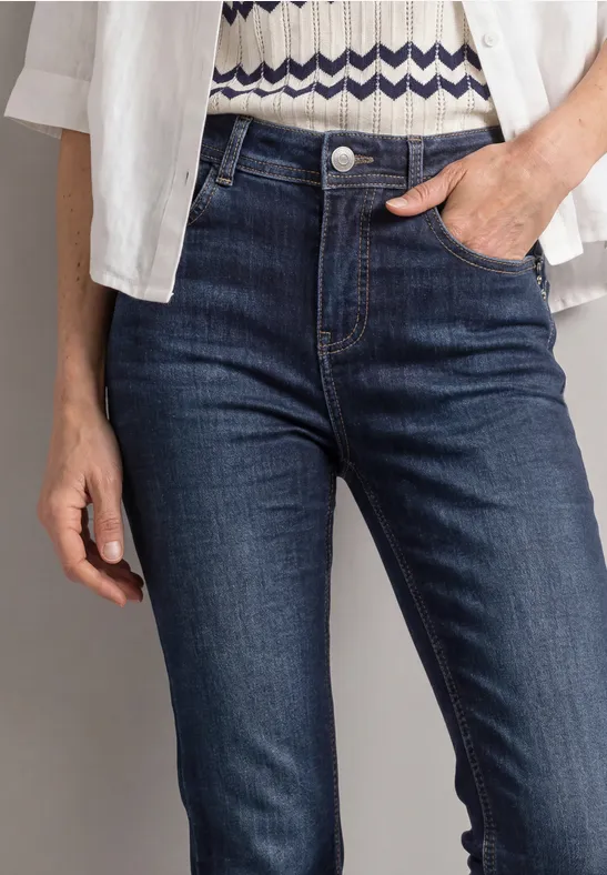 Gros plan d'une personne en jean bleu foncé, main dans la poche, chemise blanche et top à motifs.