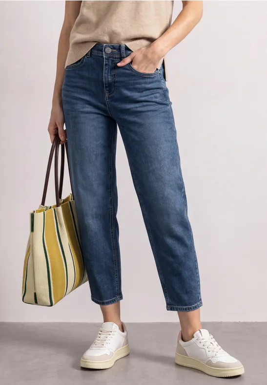 Vrouw in beige shirt, blauwe rechte jeans, witte sneakers en gestreepte shopper.