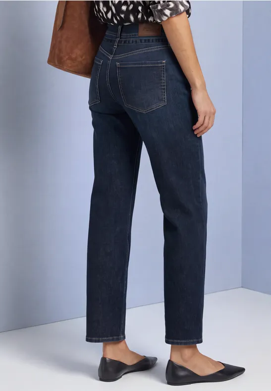 Vrouw draagt een rechte, donkerblauwe jeans en zwarte ballerina's, alleen het onderlichaam is zichtbaar.