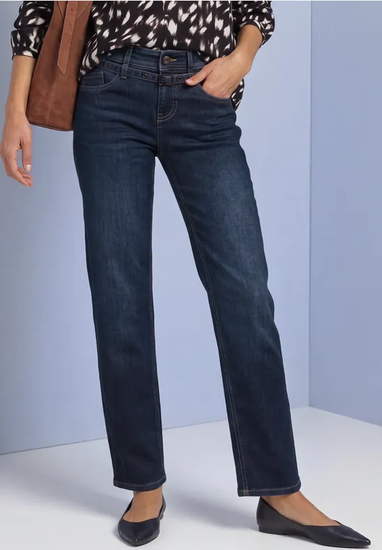 Vrouw draagt recht gesneden donkerblauwe jeans met hoge taille, zijzakken en zwarte puntige ballerina’s.