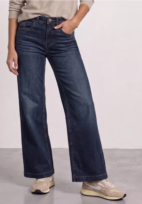 Eine Person trägt weite, dunkelblaue Jeans und helle Sneaker.