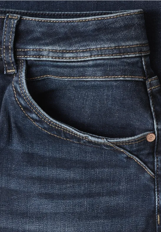Nahaufnahme einer dunkelblauen Jeans: Fronttasche, Ziernähte und Metallknopf.