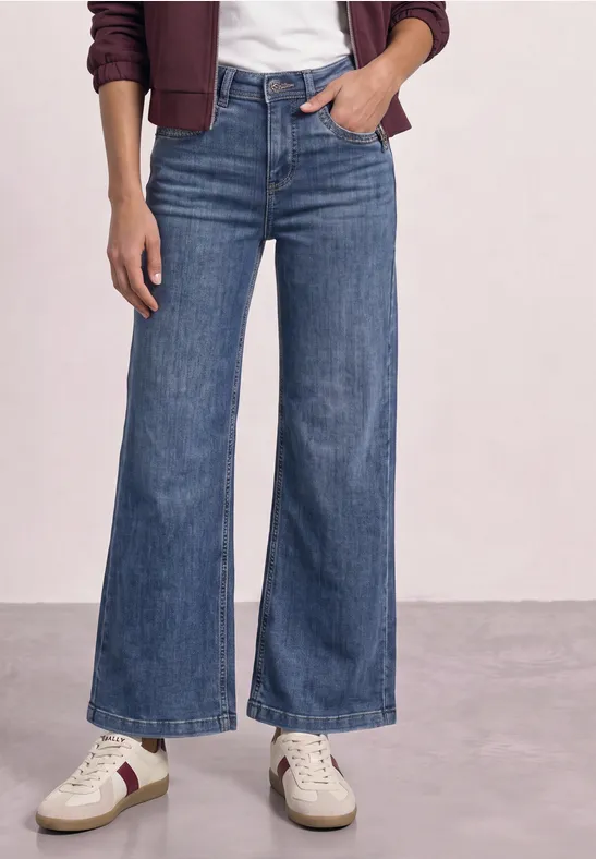 Femme portant un jean taille haute à coupe large, baskets blanches et veste bordeaux.