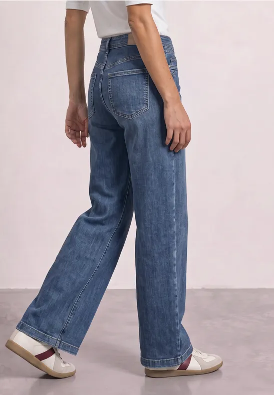 Jean taille haute en denim bleu, coupe large, porté avec des chaussures blanches.