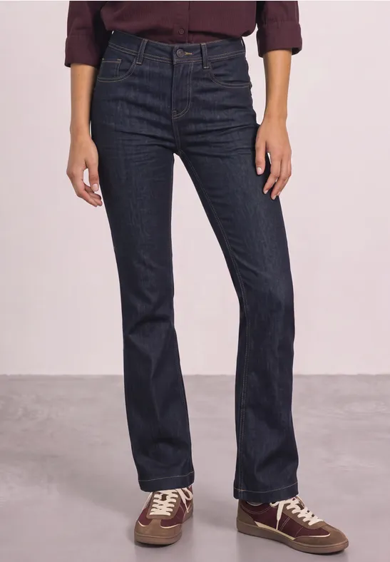 Jean taille haute bleu foncé, coupe évasée aux jambes, porté avec chemise bordeaux et baskets décontractées.