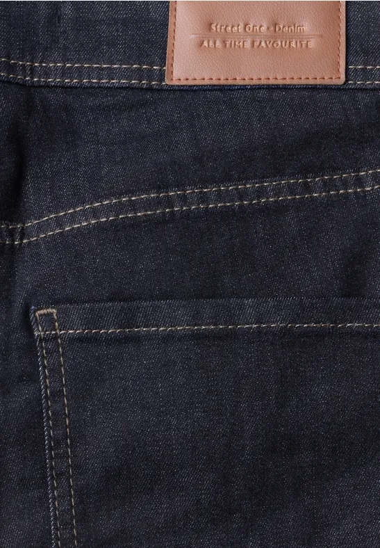 Gros plan d’un jean bleu foncé avec écusson en cuir brun et surpiqûres jaunes sur la poche arrière.