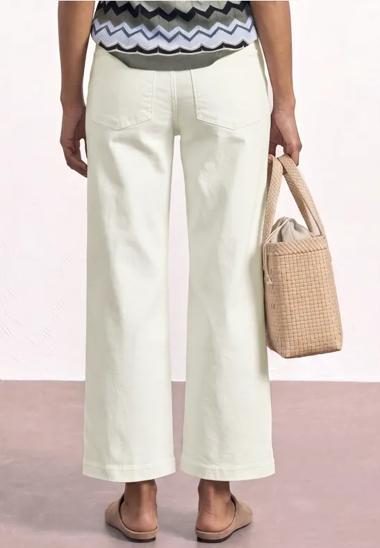 Vrouw van achteren in witte wijde broek, gemêleerde top, sandalen en strooien tas