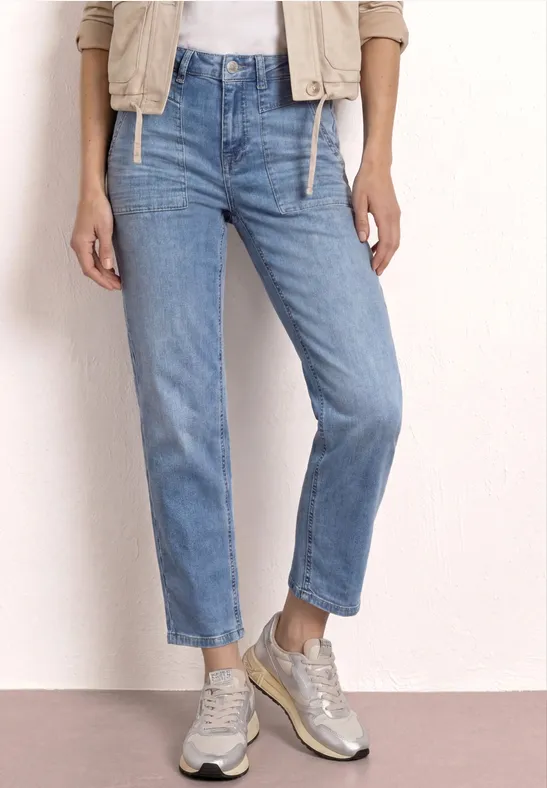 Jambes en jean bleu clair et baskets claires devant un fond neutre.