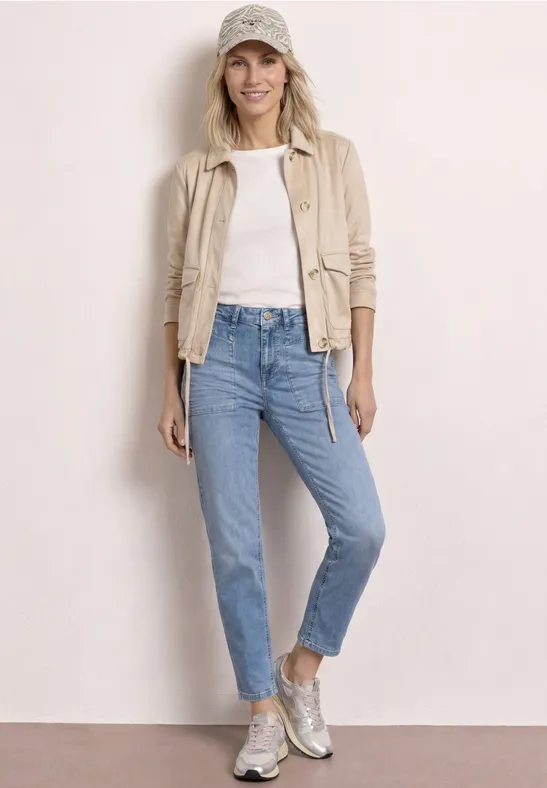 Femme en veste beige, t-shirt blanc, jean bleu clair, baskets argentées et casquette.