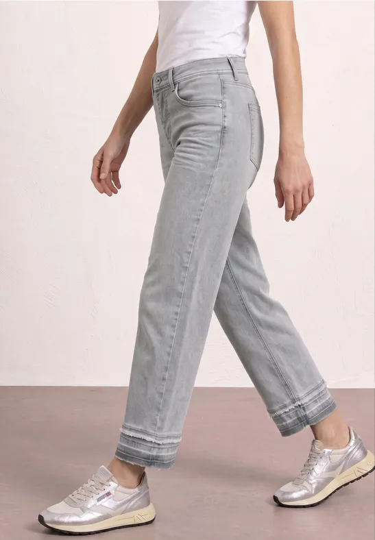 Vue latérale d'une personne portant un jean gris clair retroussé aux chevilles et des baskets argentées.