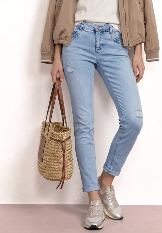 Personne en jean bleu clair, veste beige et baskets, tenant un panier tressé en paille.
