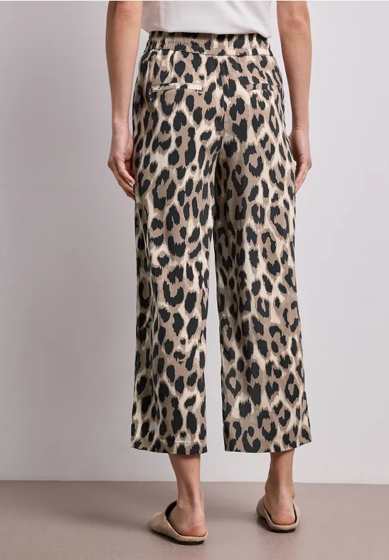 Pantalon large imprimé léopard arrivant aux chevilles, porté avec des sandales simples sur fond neutre.