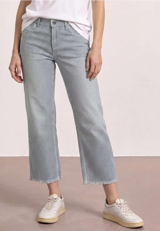 Jean droit clair, taille normale, ourlets effilochés, coupe courte, porté avec des baskets blanches.