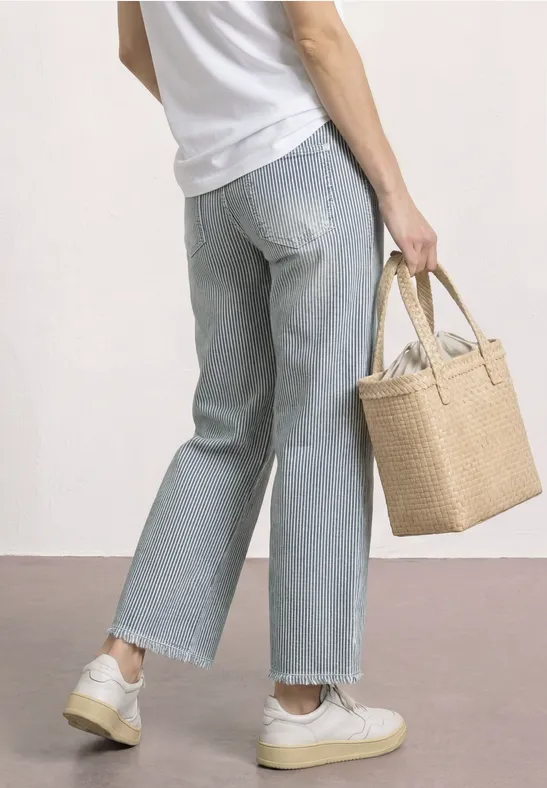 Vue arrière d'une personne en jean large, t-shirt blanc et baskets, tenant un panier tressé.