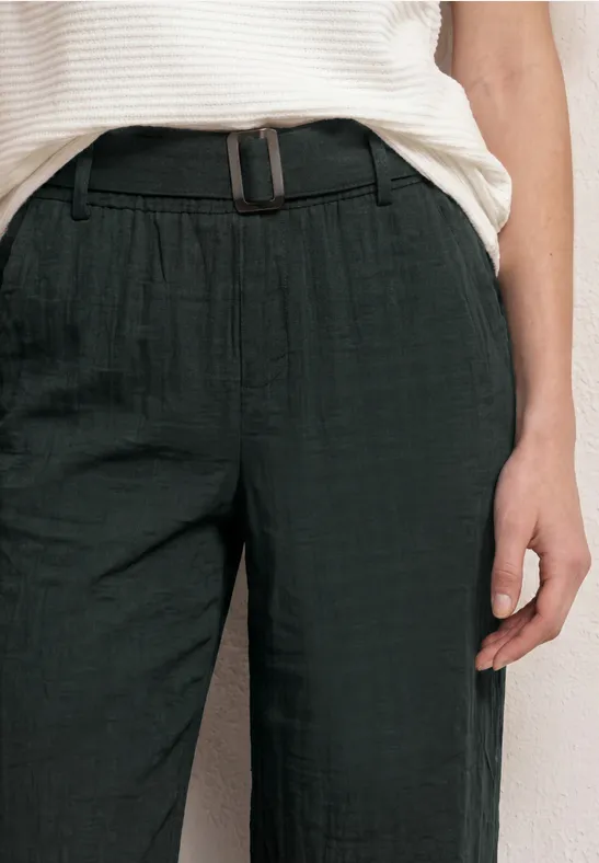 Donkere linnenbroek met elastische taille en smalle riem, gecombineerd met een wit bovenstuk.