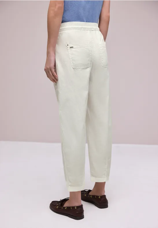 Vue de dos d’une personne portant un pantalon blanc ample et des mocassins marron.