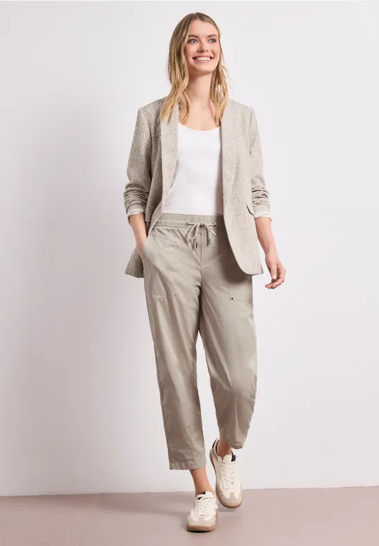 Une femme porte un pantalon en lin beige, un ensemble blazer blanc, top blanc et baskets blanches.