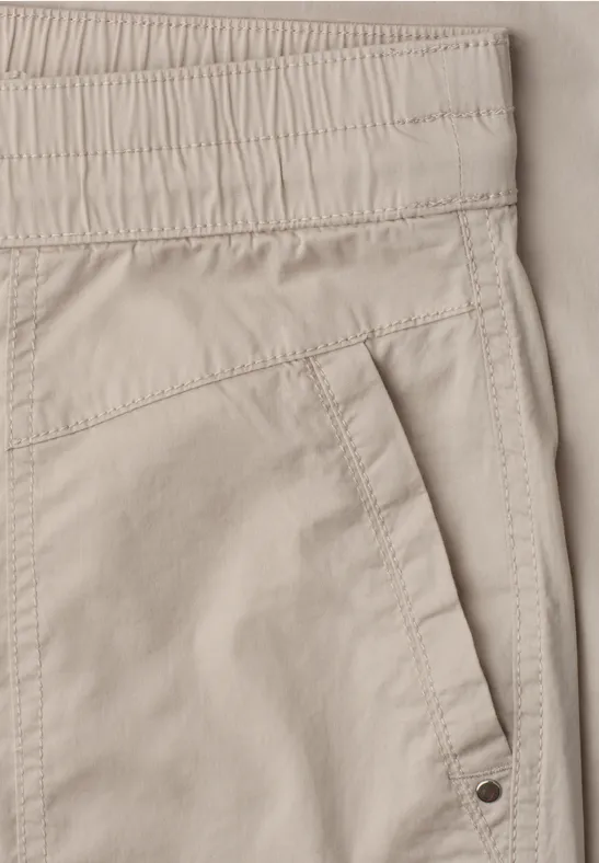 Pantalon beige avec taille élastique et poche latérale oblique.