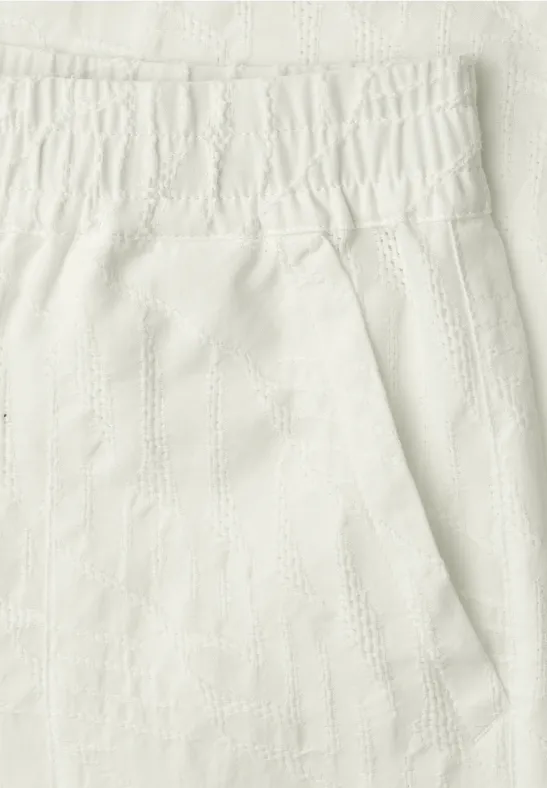 Close-up van een witte, gestructureerde stof met elastische tailleband en een zak