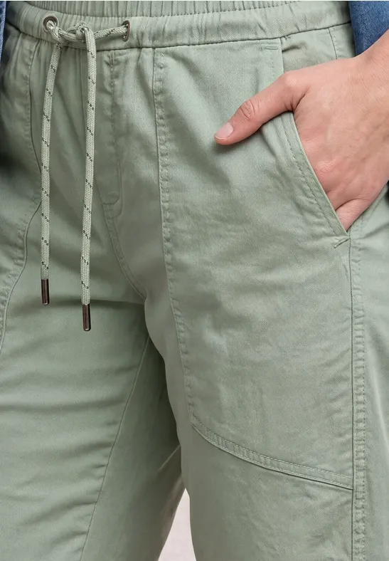 Close-up van een lichtgroene broek met trekkoord en hand in de voorzak.