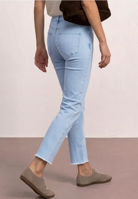 Persoon draagt een lichtblauwe jeans, bruine instappers en een bruine schoudertas voor een lichte achtergrond.