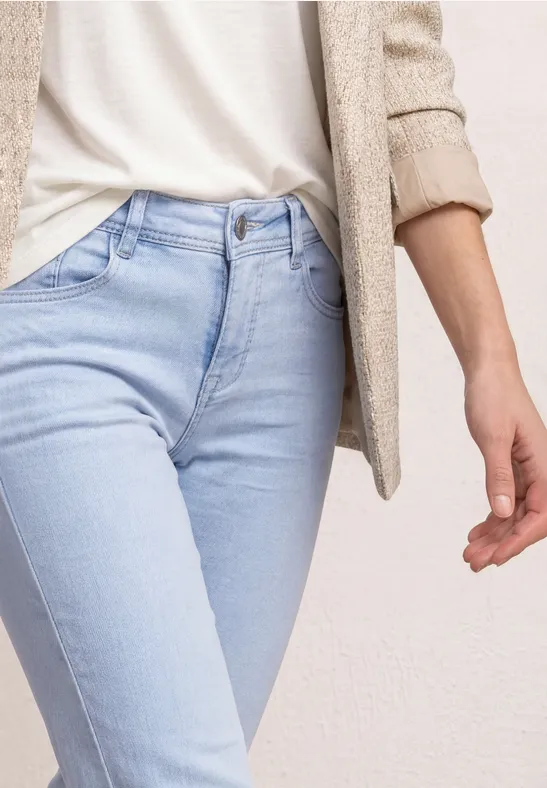 Close-up van het bovenlichaam met lichtblauwe jeans, wit shirt en beige blazer.