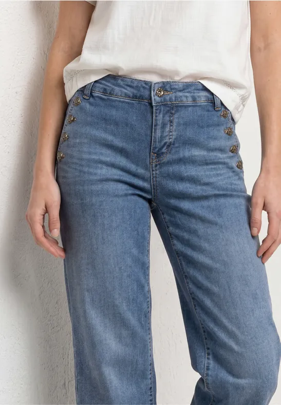 Gros plan sur une personne portant un jean taille haute bleu clair et un haut blanc devant un mur clair.